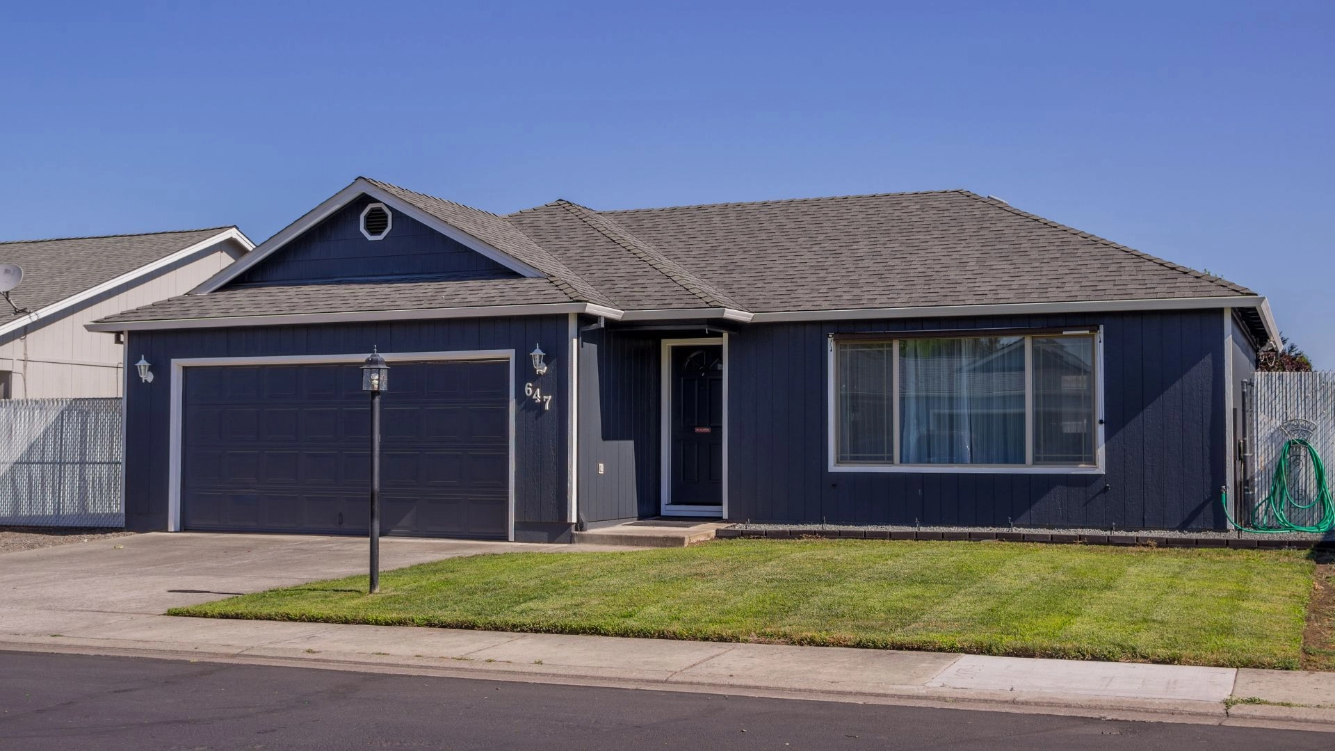 A house with a garage and a well-maintained lawn under a clear sky. The structure features windows and siding, with a visible door and garage door.